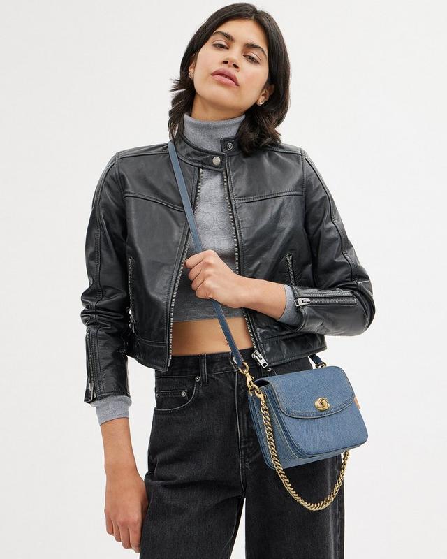 a woman in a leather jacket and jeans holding a blue cross body bag