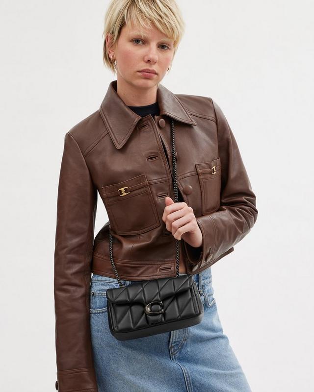 a woman in a brown jacket holding a black purse
