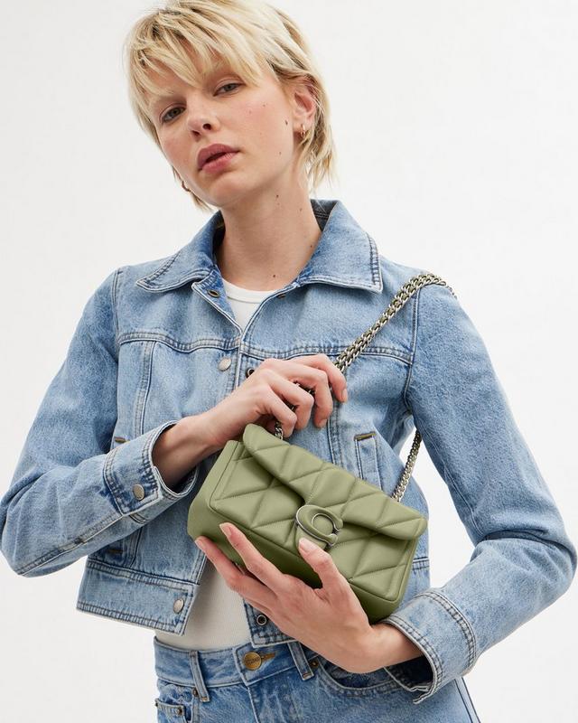 a woman in a denim jacket holding a green purse