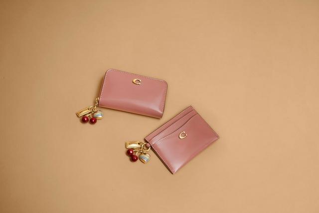 Pink leather wallet and card holder with cherry charm attachments displayed together.