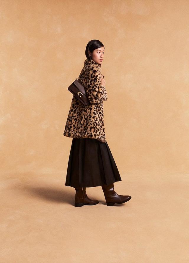 Model wearing leopard print coat, black midi skirt, brown boots, and carrying a brown leather handbag.