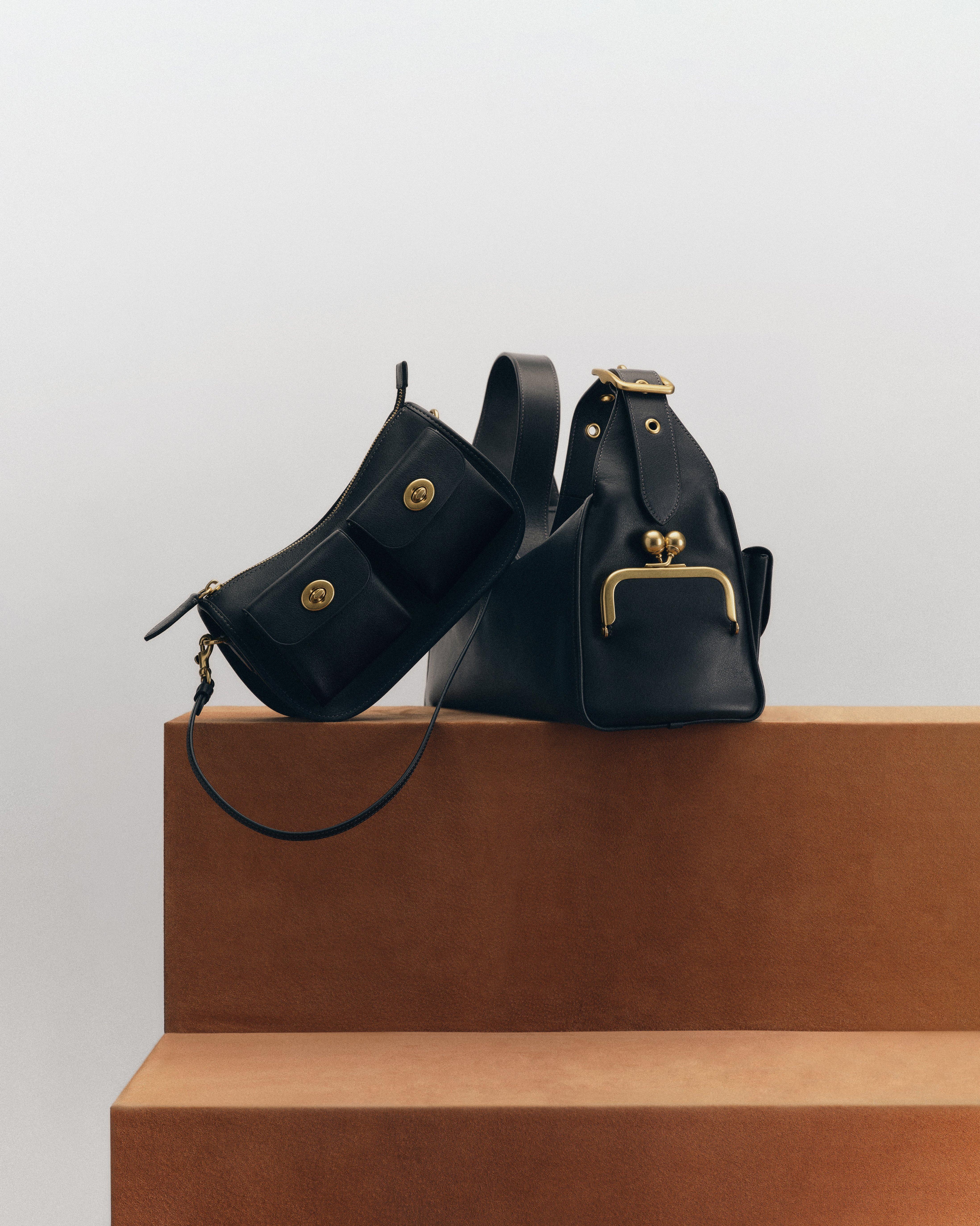 Two black mini bags styled on a tan plinth