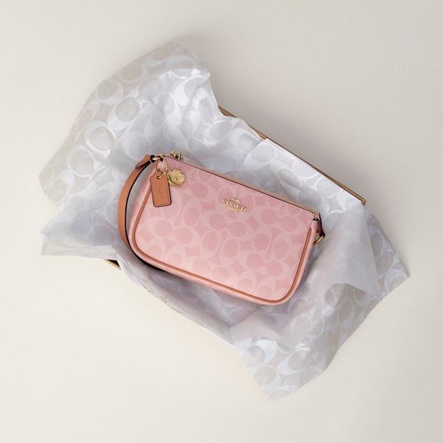 Pink Coach wristlet with gold hardware and charm, displayed on branded tissue paper.