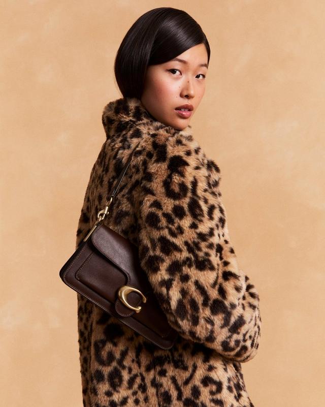 Model wearing leopard print faux fur coat, carrying a brown leather shoulder bag with gold hardware.