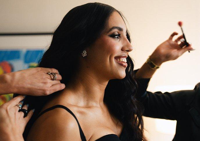 Woman smiling while having makeup applied and hair styled by professionals.