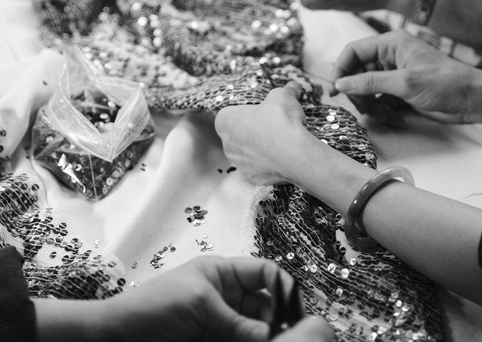 Hands applying sequins to embellished fabric during garment embellishment process.