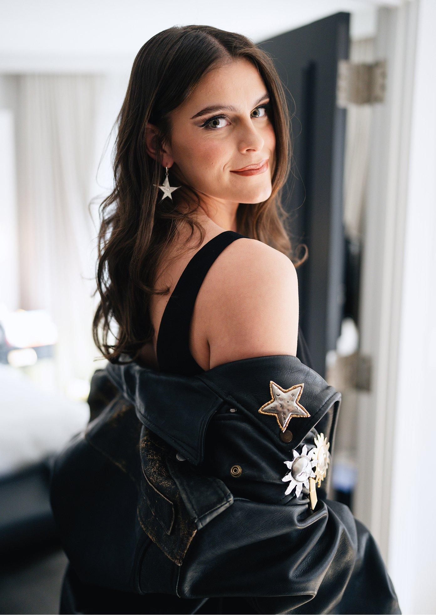 Woman wearing star-shaped earrings and a black leather jacket with decorative star and sun brooches.