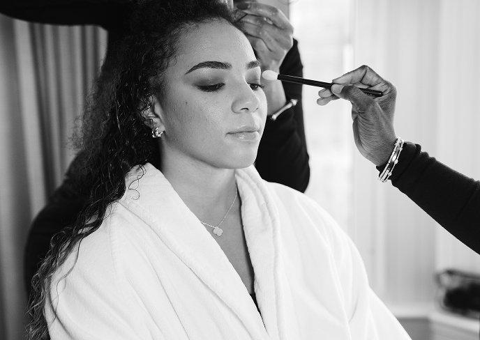 Woman having eye makeup applied by makeup artist while wearing a white robe.