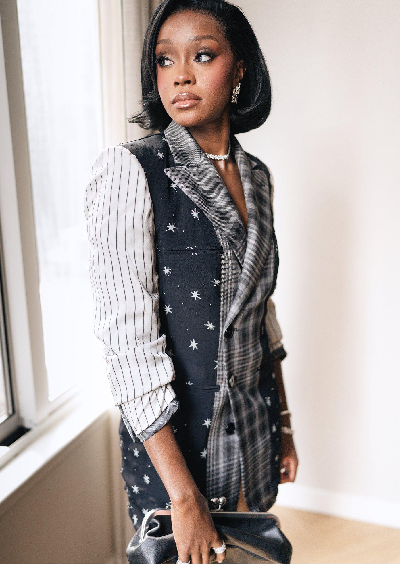 Woman wearing mixed-pattern blazer with striped sleeve, plaid and star-print panels, paired with pearl necklace.
