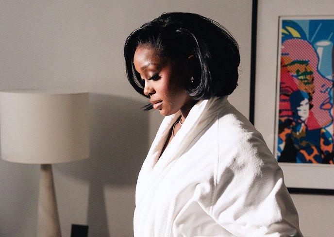 Woman in white bathrobe looking down in a relaxed indoor setting.