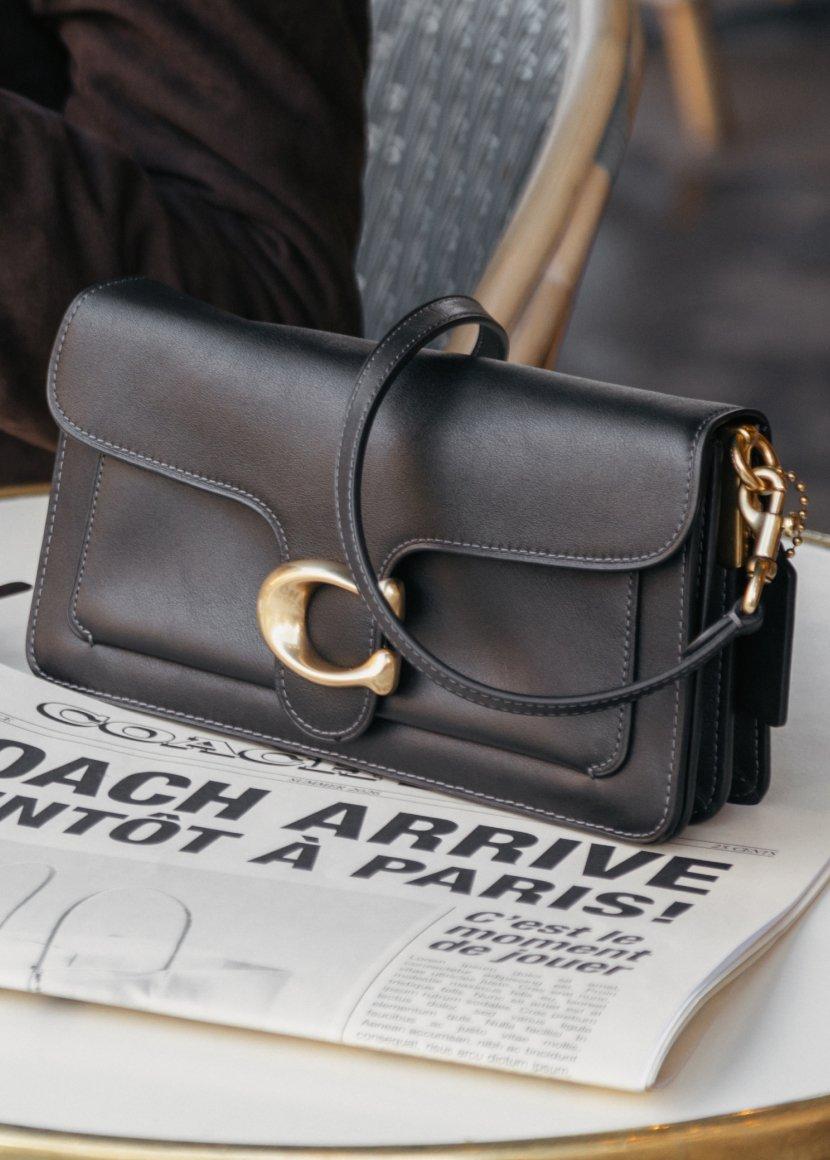 a black purse sitting on top of a table with a newspaper