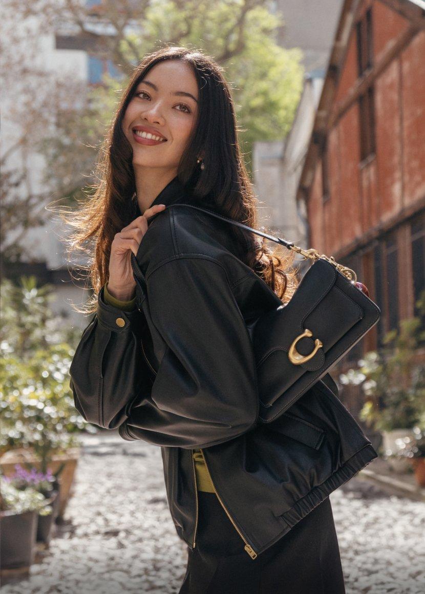 a woman in a black jacket holding a purse on a cobblestone street