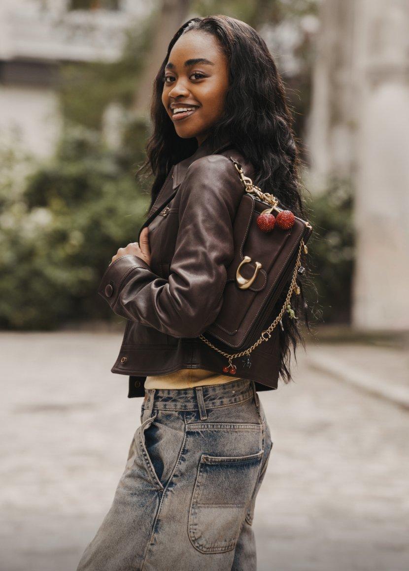 a woman in a leather jacket and jeans holding a purse