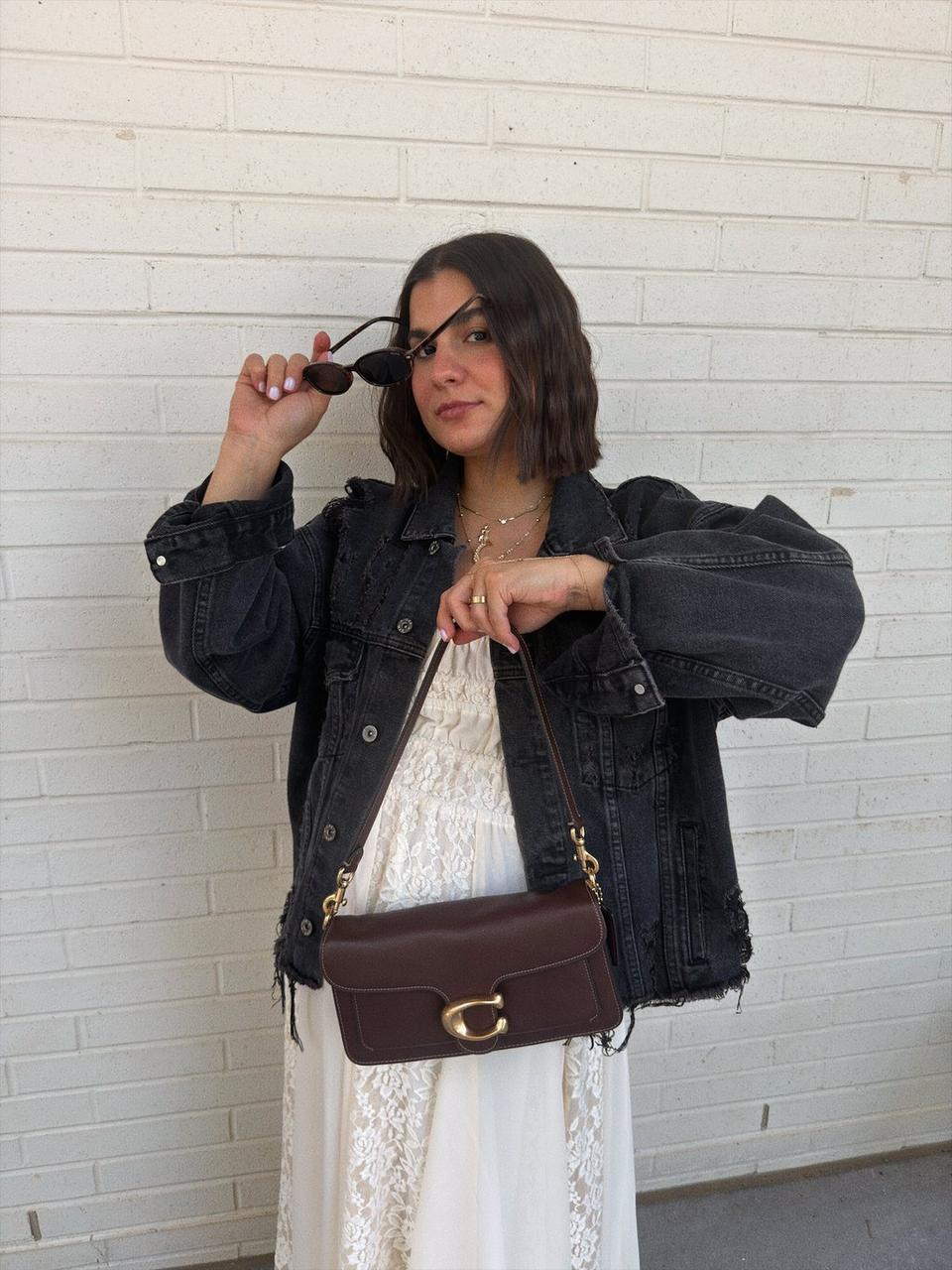 Model standing with shoulder bag at a rooftop dinner