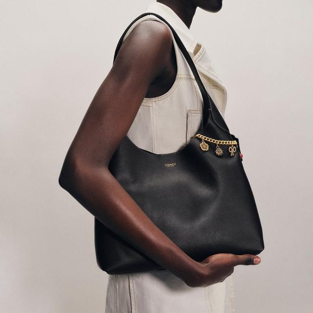 Model wearing a beige sleeveless top carrying a black leather Coach shoulder bag with gold chain detail.