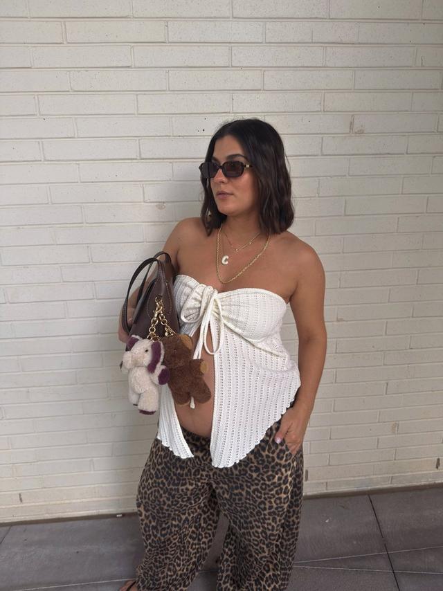 Woman wearing white strapless knit top with tie detail and leopard print pants, holding a brown handbag.