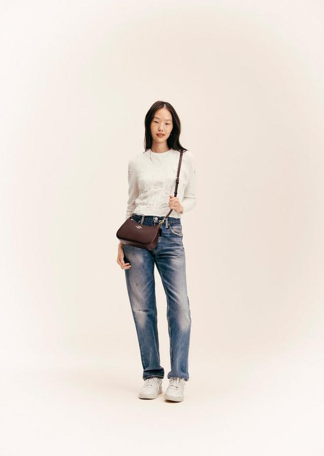 Model wearing white long-sleeve top, distressed blue jeans, and carrying a brown crossbody bag.