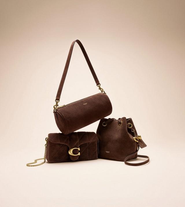 Three brown Coach handbags with gold hardware stacked together, including a barrel bag, shoulder bag, and drawstring bucket bag.