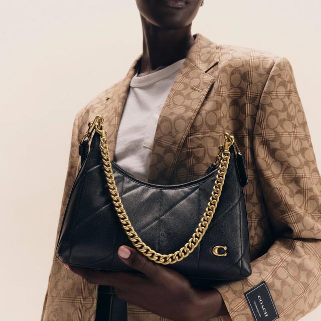 Model wearing tan plaid Coach blazer holding black leather hobo bag with gold chain strap.
