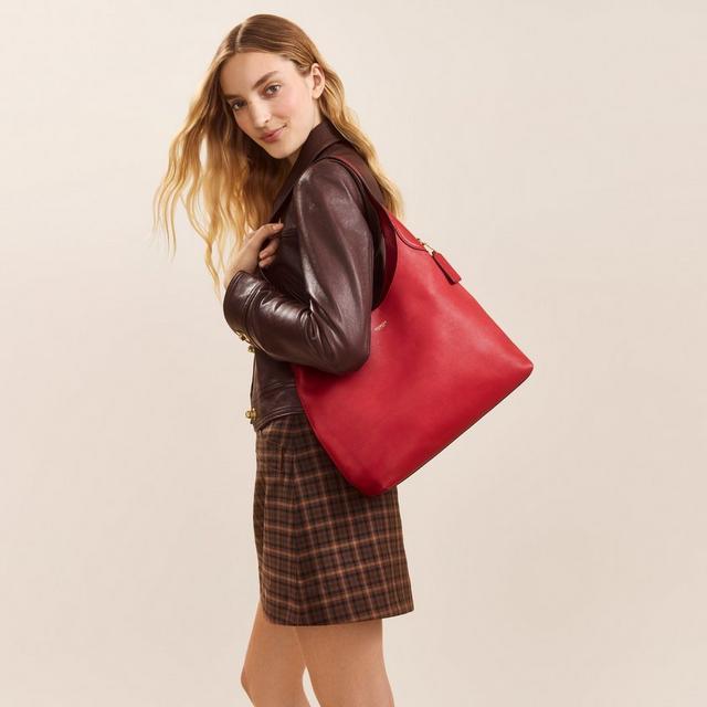 Woman wearing brown leather jacket and plaid skirt carrying a red shoulder bag.