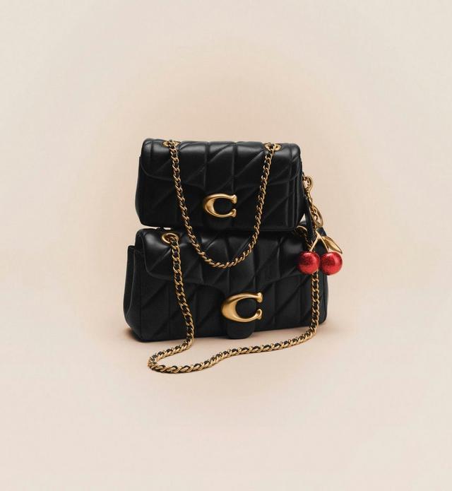 Two black quilted leather handbags with gold chain straps and C logo hardware, with red cherry charm.
