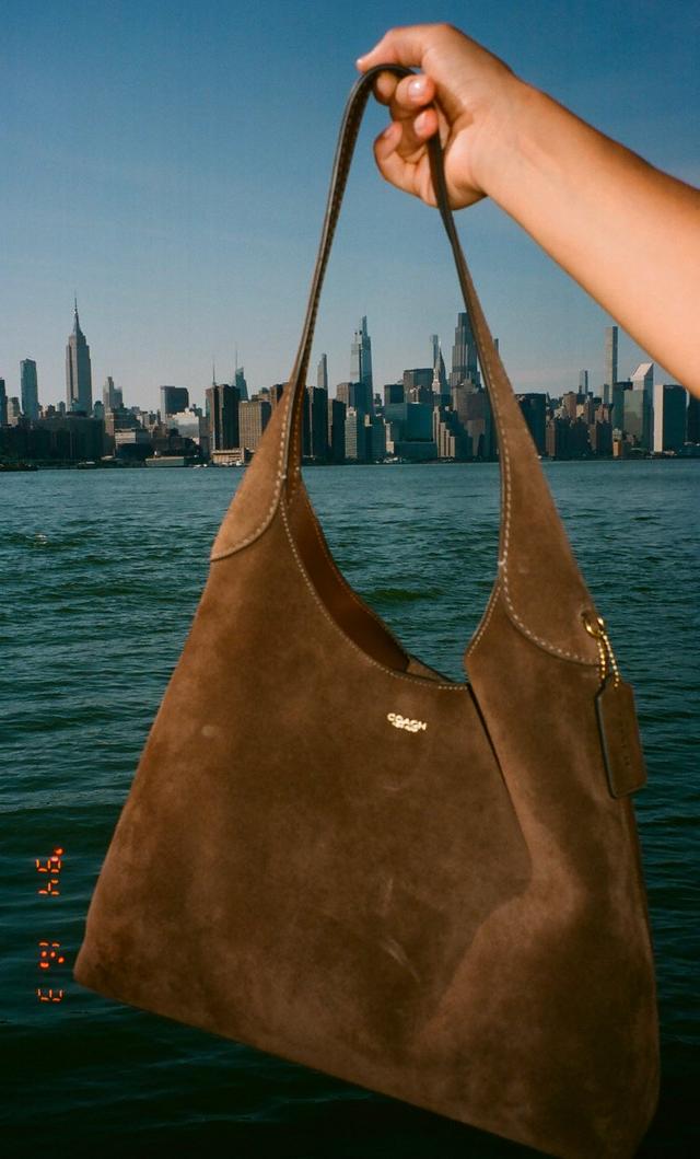 Model holding brown suede Coach hobo bag outdoors with close-up detail view of the bag.