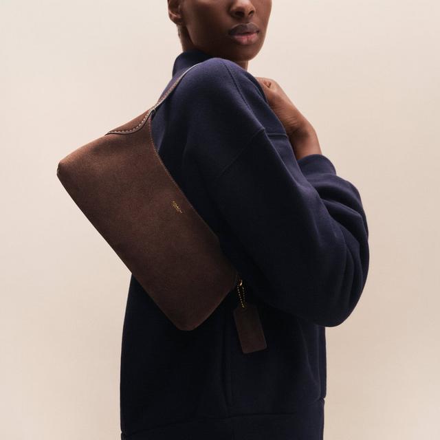 Model wearing a black leather jacket holding a Coach monogram crossbody bag with gold chain strap.