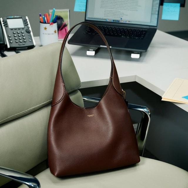Coach brown leather hobo bag with single shoulder strap positioned on office desk chair.