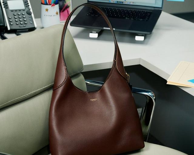 Coach brown leather hobo bag with single shoulder strap positioned on office desk chair.