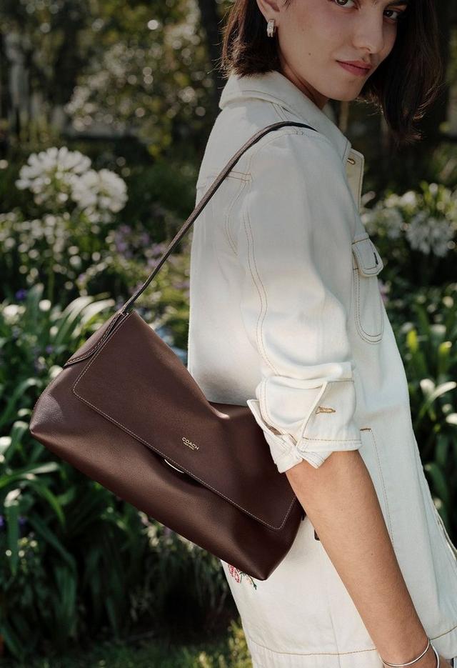 a woman is holding a brown purse in the grass