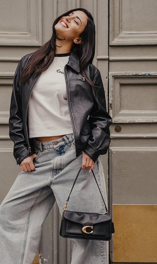 a woman in a black leather jacket and jeans posing for a photo