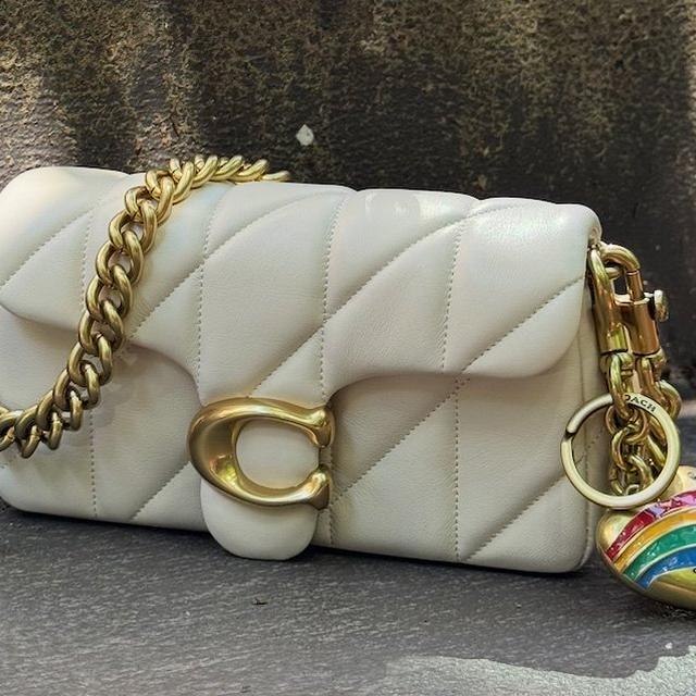Cream quilted Coach shoulder bag with gold chain strap and rainbow heart charm attached.