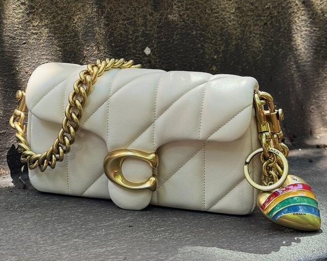 Two cream quilted Coach handbags with gold chain straps and decorative charms displayed on steps.