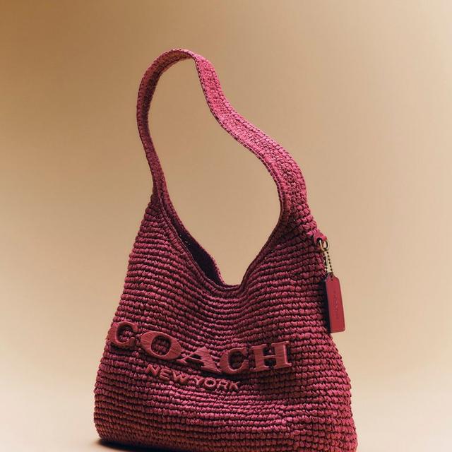 Coach burgundy woven shoulder bag with embossed logo text and leather tag charm.