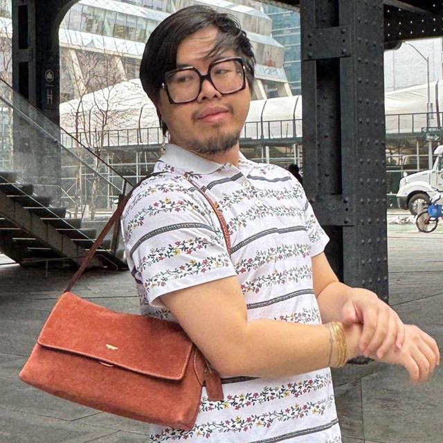 Person wearing oversized square glasses, white floral striped polo shirt, and brown crossbody bag outdoors.