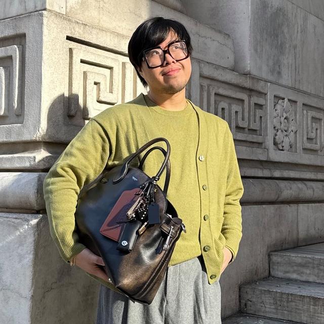 Person wearing oversized black eyeglasses and yellow cardigan holding a multicolored leather handbag.