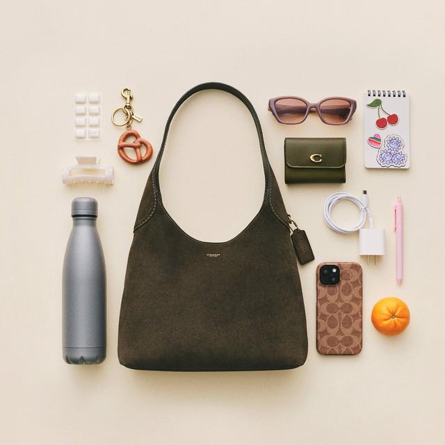 Olive green Coach shoulder bag surrounded by accessories including sunglasses, wallet, water bottle, and phone.