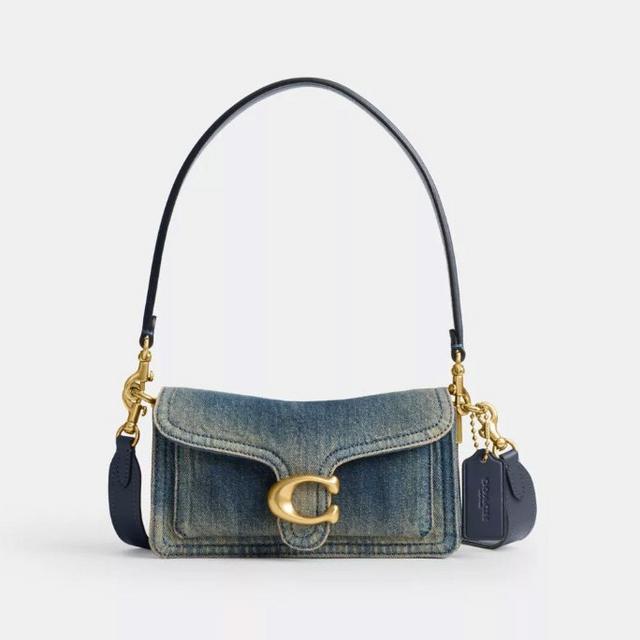 Small denim shoulder bag with gold C-shaped hardware closure and navy leather strap with charm details.