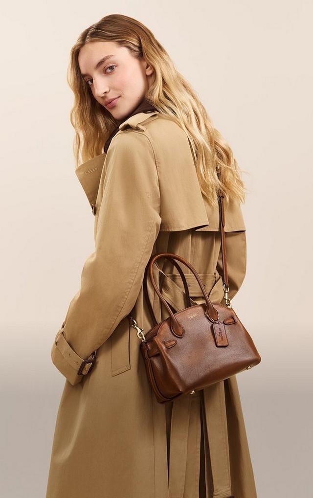 Deux mannequins portant le cabas Coach Empire 21 en cuir vieilli, l’une avec un trench beige, l’autre un sweat bleu marine.