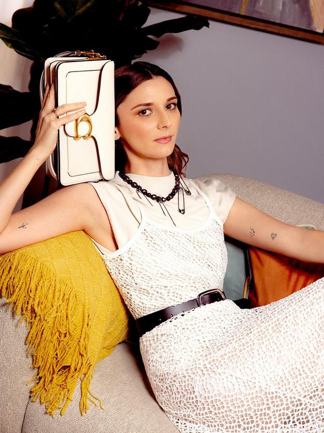a woman standing in a room holding a white purse