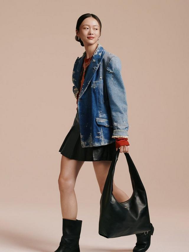 Woman wearing a distressed blue denim jacket over a rust-colored top with gold jewelry and earrings.