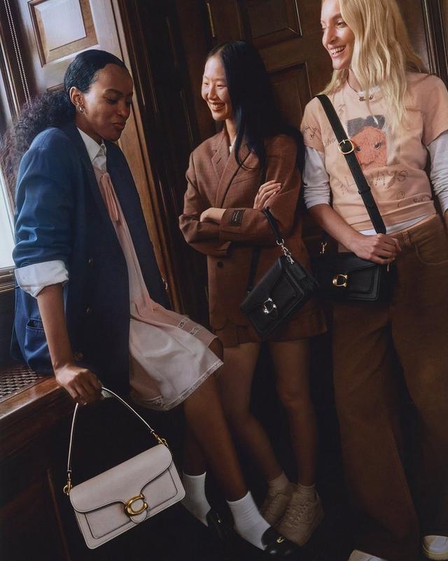 three women are sitting on a bench and holding purses