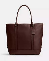 Burgundy leather tote bag with dual handles and a Coach brand tag.