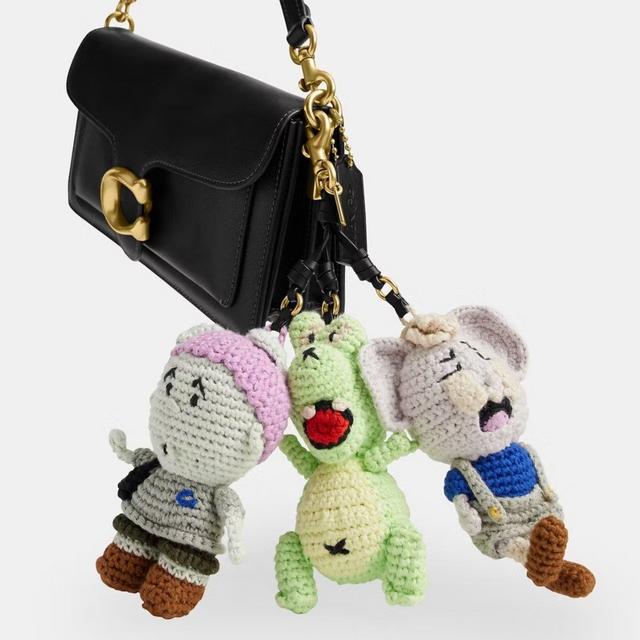 A black bag with a gold C-shaped clasp. It features a three-dimensional charm made of bundled crochet mascots from Coach | Brain Dead.